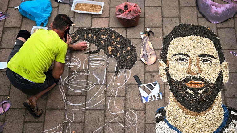 Kosovar artist Alkent Pozhegu works on a mosaic on the ground, made with grain and seeds, and depicting Argentina's forward #10 Lionel Messi (R) and Spain's forward #19 Lamine Yamal, in the town of Gjakova on July 16, 2026. Thousands of kilometres away from New York, where the Argentina and Spain football teams will compete for the World Cup title, in the western city of Gjakova, Alkent Pozhegu has made a mosaic depicting the two forward stars Lionel Messi and Lamine Yamal. (Photo by Armend NIMANI / AFP) / RESTRICTED TO EDITORIAL USE - MANDATORY MENTION OF THE ARTIST UPON PUBLICATION - TO ILLUSTRATE THE EVENT AS SPECIFIED IN THE CAPTION