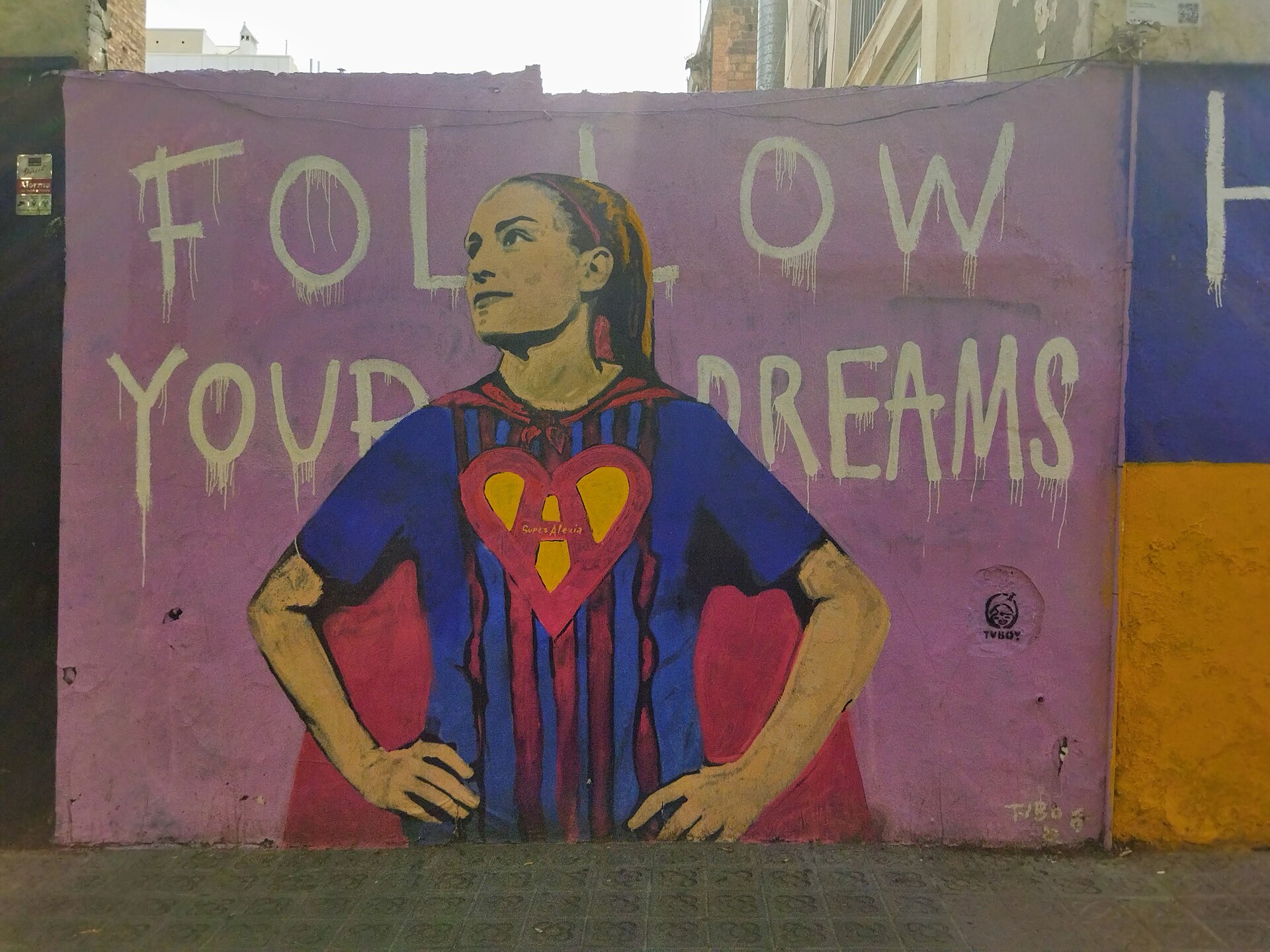 The mural shows soccer player Alexia Putellas Segura. Behind the image of her, the following phrase in English is shown: "Follow your dreams". The player wears a Barcelona Football Club shirt and a superwoman cape, on the shirt as a shield the letter "A" is printed, which represents the player's name. The mural is located in the Gracia neighborhood of Barcelona.