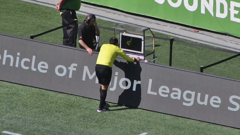 Referee Baldomero Toledo consults the video assistant referee during a Major League Soccer match between Seattle Sounders FC and Sporting Kansas City at CenturyLink Field . The review resulted in a red card for Sounders defender Chad Marshall .